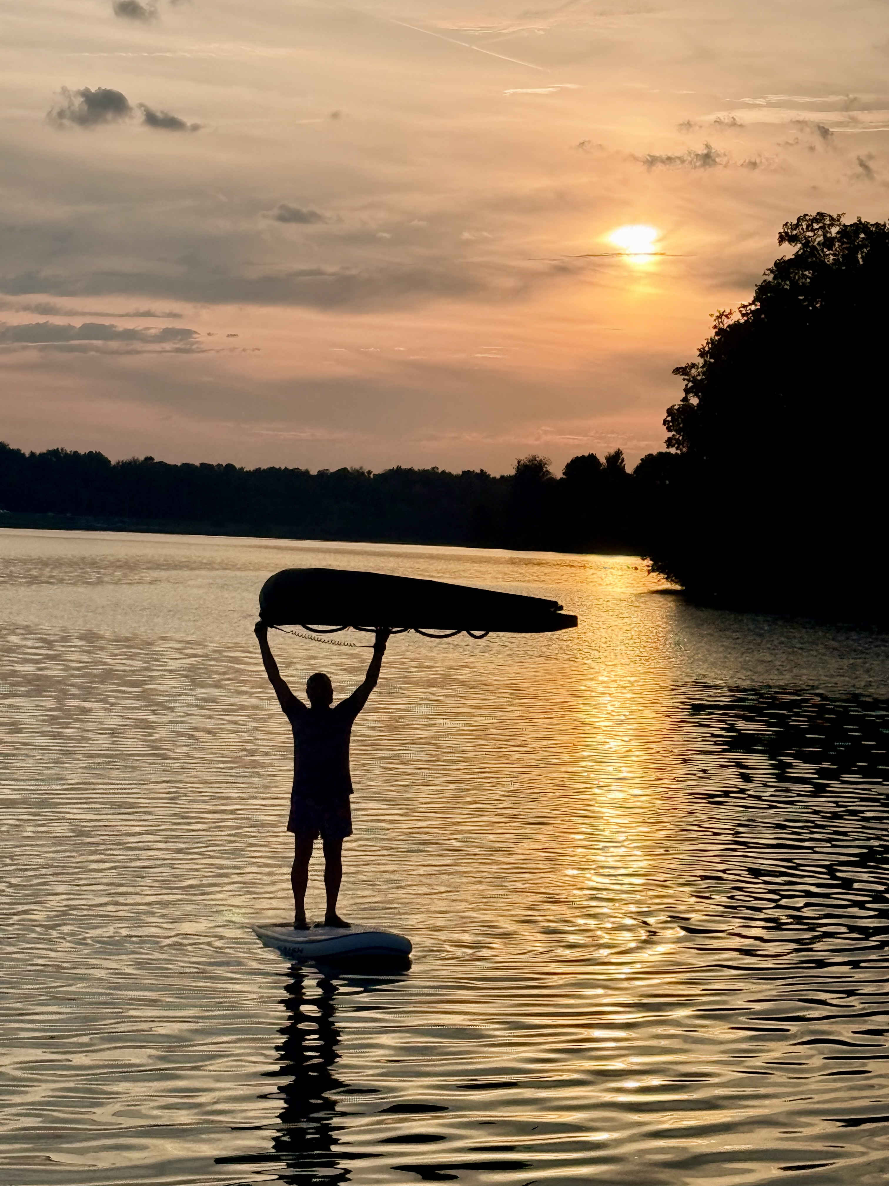 Doychin standing on a board at sunset, holding his wing overhead on calm water