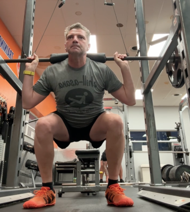 Doychin performing a squat in a gym with a bar across his shoulders